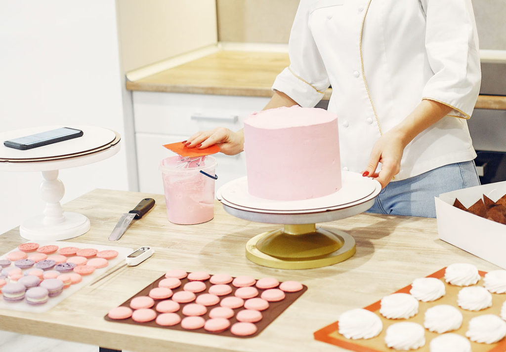 A person icing a cake in pink buttercream