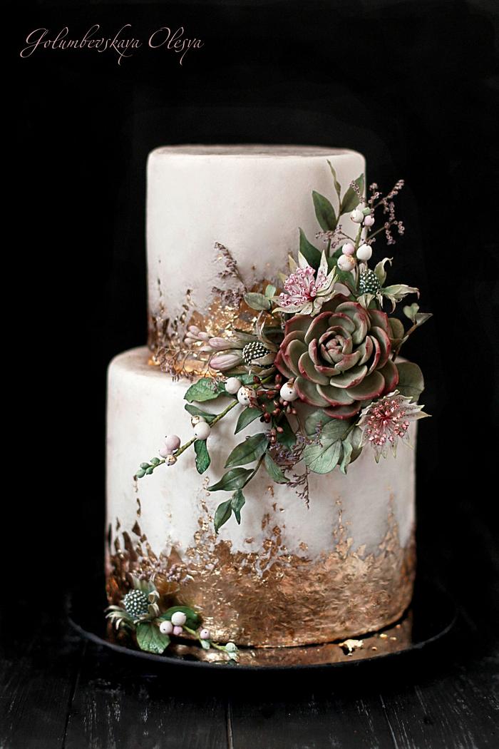 Two tier white cake with fondant adorn with gold leaf and a spray of green foliage and a large succulent 